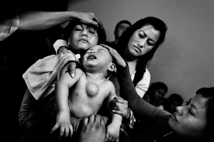 A Colombian mother holds her baby boy, having a tumor in his chest, during the religious healing ritual performed at a house church in Bogota, Colombia.