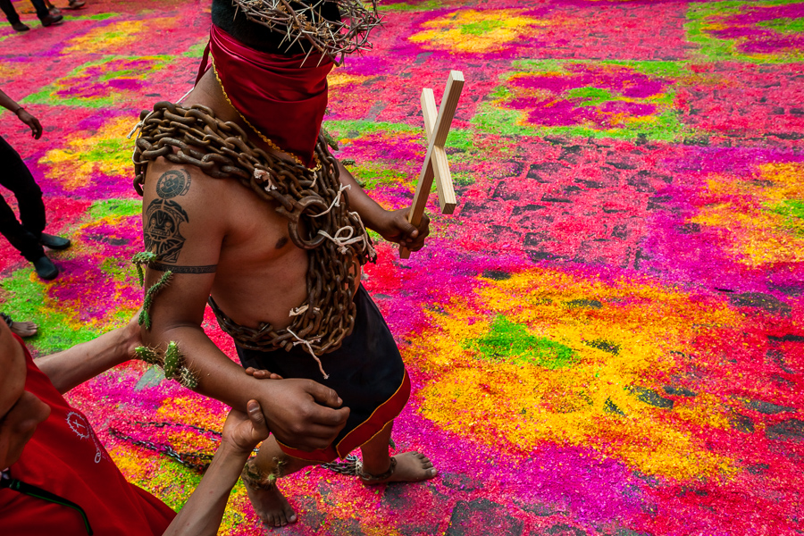 A hooded penitent, wearing chains and cactus spines stuck to his arm, walks on a colorful sawdust carpet during the Holy week procession in Atlixco, Mexico.