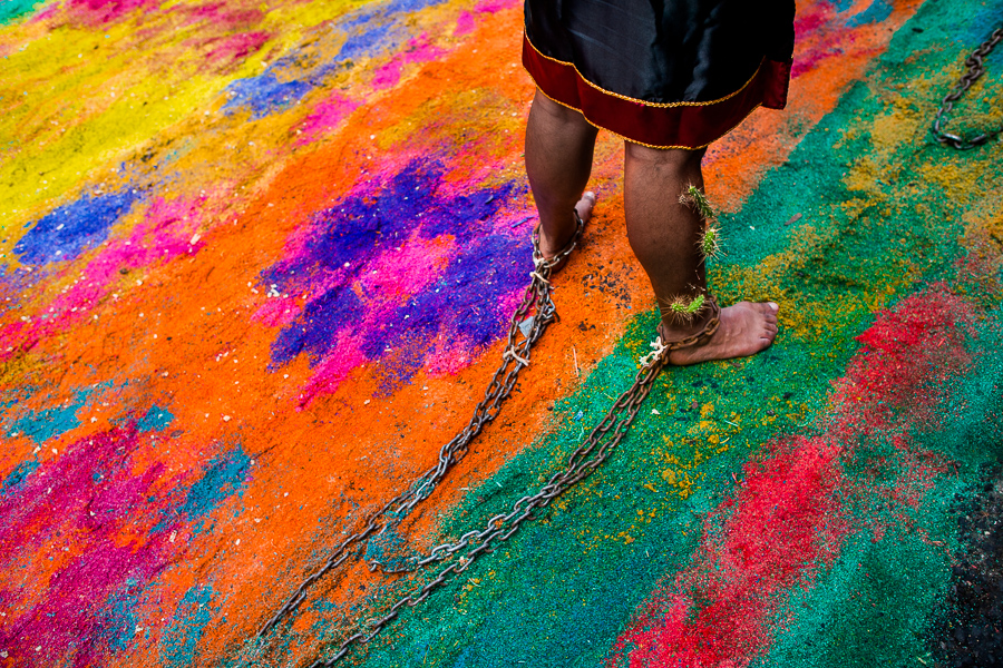 A chained Catholic devotee, with cactus spines stuck to his legs, walks on a colorful sawdust carpet during the Holy week penitential procession in Atlixco, Mexico.