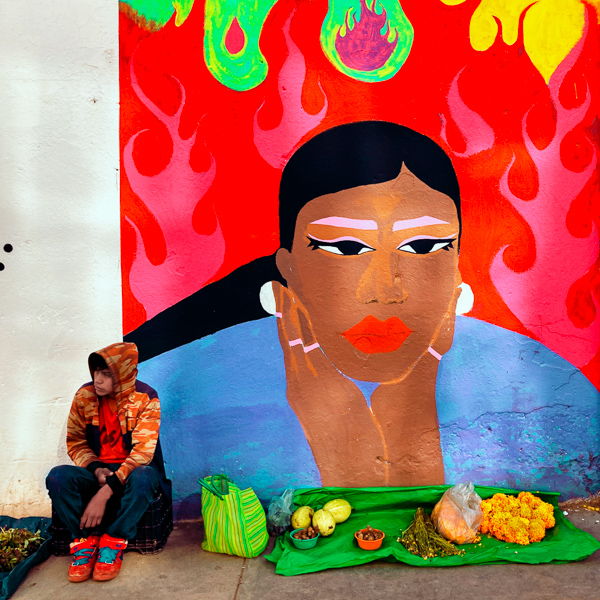 A Mexican indigenous boy sells homegrown vegetables and herbs in front of a large street mural in Tlapa de Comonfort, Guerrero, Mexico.