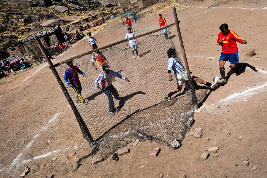 Indigenous men play football on a dirt football pitch in the rural mountain community close to Puno, Peru.