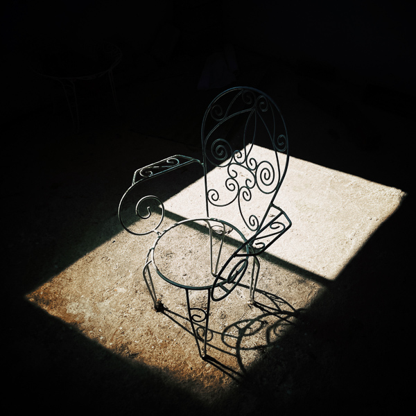 A wrought iron chair is seen placed in a rectangle of light coming through a window.