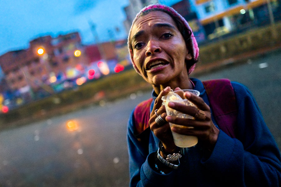 A young Colombian woman, living on the street and smoking “bazuco”, hangs out in front of an asylum center during a rainy twilight in Medellín, Colombia.