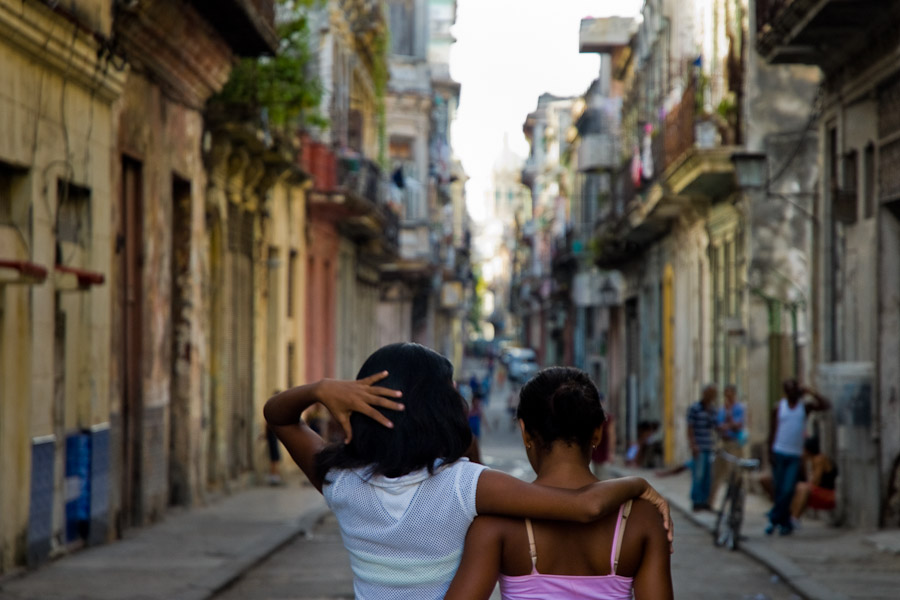 Young Cuban girls walking embraced down the lively street in the Havana downtown during the dusk, Cuba.