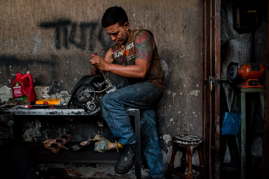 A Colombian car mechanic works on an engine in a car repair workshop in Barrio Triste, Medellín, Colombia.