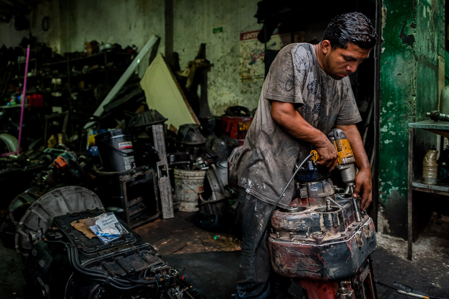 A Colombian car mechanic works on a transmission housing in a car repair shop in Barrio Triste, Medellín, Colombia.
