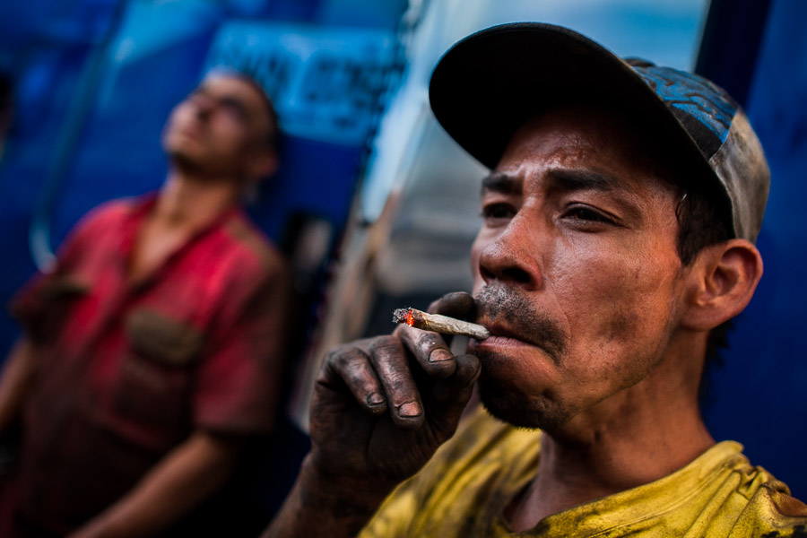 A Colombian car mechanic smokes a marijuana cigarette during a short work break in Barrio Triste, Medellín, Colombia.