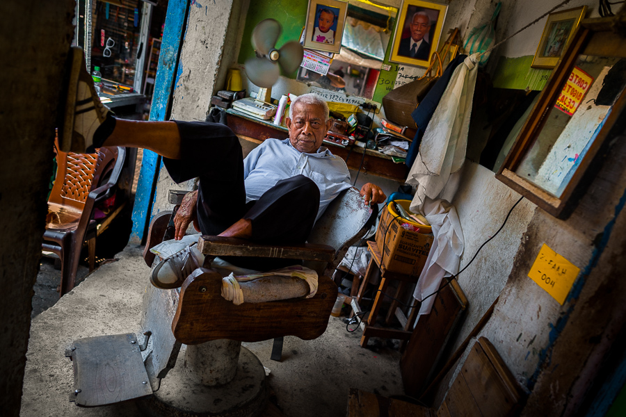 A Colombian hairdresser sits in a wooden armchair while waiting for the customers in his barber shop in the market of Bazurto in Cartagena, Colombia.