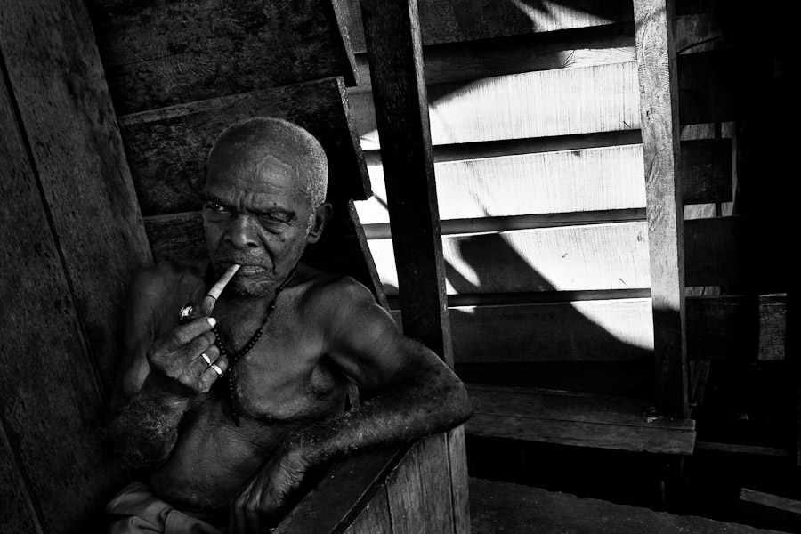 An old man smokes pipe on the porch of his wooden house in the poor neigbourhood of Tumaco, Colombia.