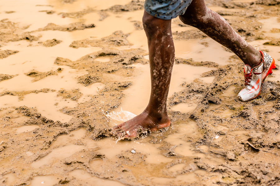 An Afro-Colombian boy, wearing only one football boot, plays football during the training session on a dirt field in Quibdó, Chocó, Colombia.