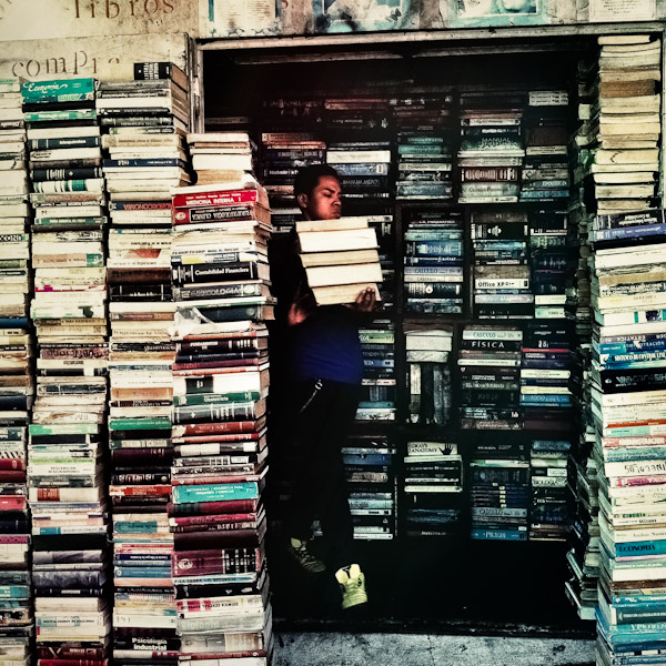 A Salvadorean book vendor carries a pile of books to sell them outdoors on the street of San Salvador, El Salvador.