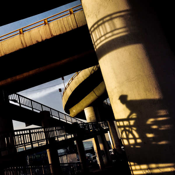 A shadow of a man riding a bicycle is seen on the pillar of the pedestrian bridge over the highway in Mexico City, Mexico.