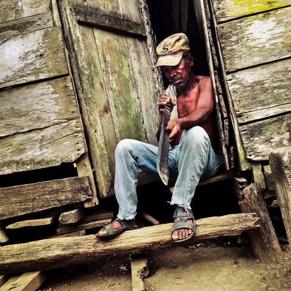A Panamanian peasant checks the sharpness of the machete blade while sitting in the door of his house in Darién, Panama.