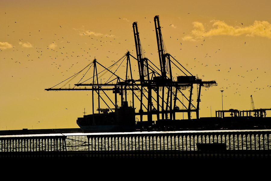 Port cranes load a cargo ship during sunset in the port of Malaga, Spain.