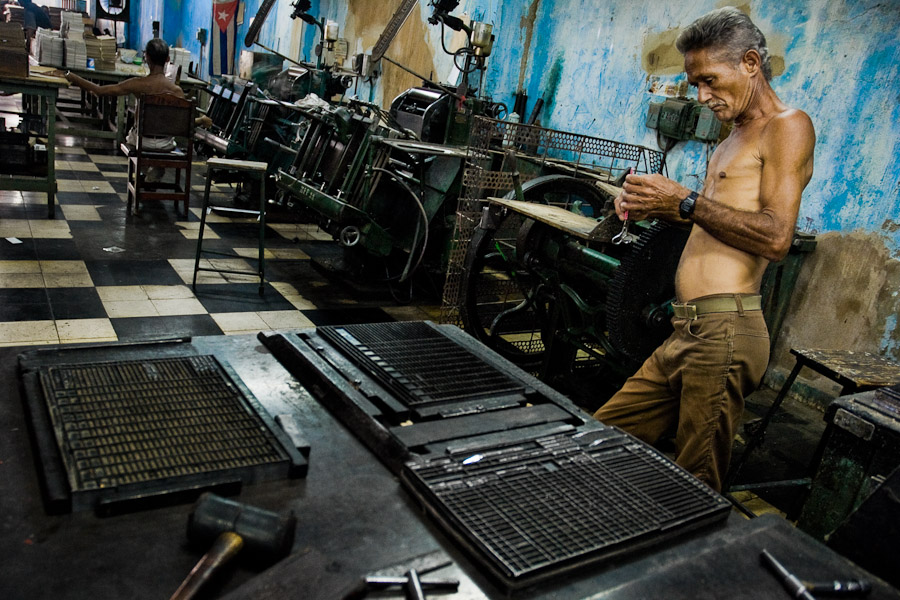 A Cuban master printer, leant against a printing machine, waiting for a new load in the state print shop, Santiago de Cuba, Cuba.