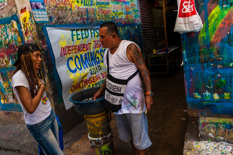 José Corredor (“Runner”) talks with a girl while clearing paint from his brushes in the sign painting workshop in Cartagena, Colombia.