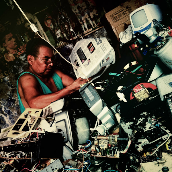 A Salvadorean TV repairman reads the morning newspaper in his workshop on the street of San Salvador, El Salvador.