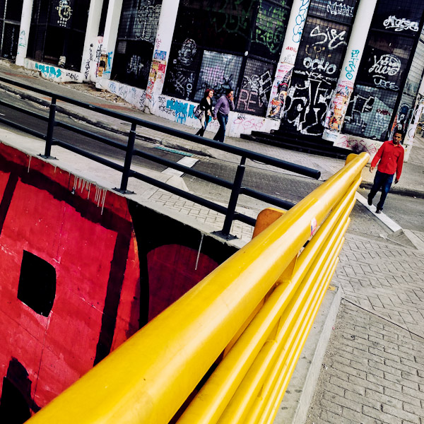 Bogotá pedestrians walk around the street corner, covered in random scrawls and territory tags, in Santa Fé, Bogotá, Colombia.