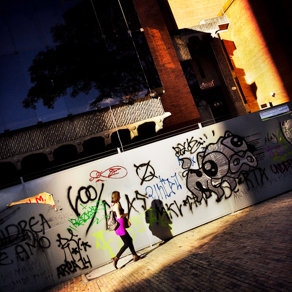 A Colombian woman passes in front of steel hoarding panels, covered in random scrawls and territory tags, in La Candelaria, Bogotá, Colombia.