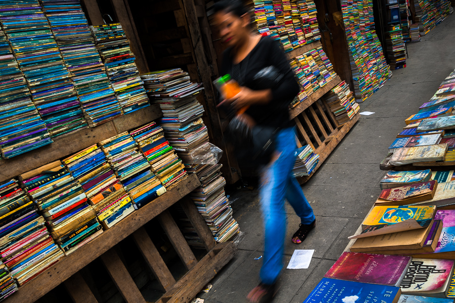 A Salvadoran woman walks along hundreds of used books stacked in shelves on the street in a secondhand bookshop in San Salvador, El Salvador.