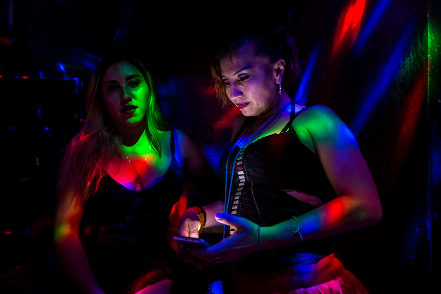 A Salvadoran sex worker looks at the phone screen while talking with her co-worker in a sex club in San Salvador, El Salvador.