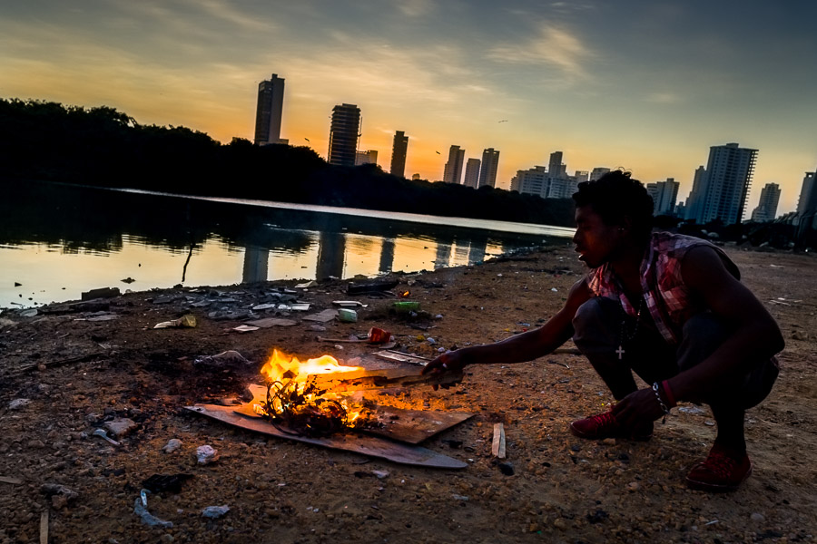 A young Afro-Colombian man burns electric wires to retrieve copper in front of a luxurious neighborhood of Cartagena, Colombia.