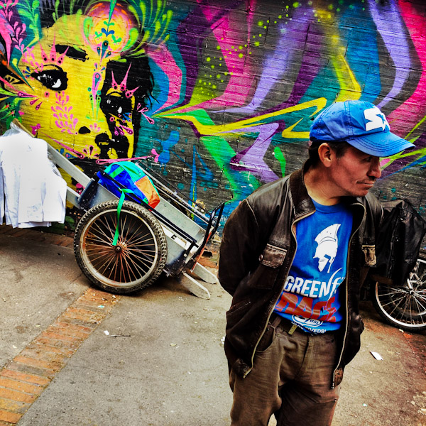 A Colombian street vendor stands in front of a graffiti artwork, created by an artist named Stinkfish, in the center of Bogotá, Colombia.