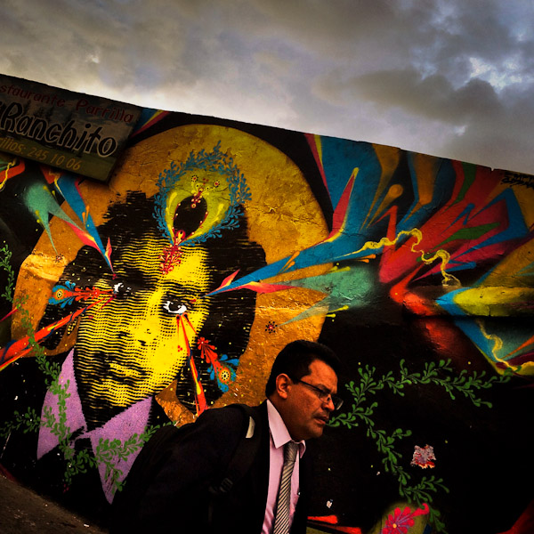 A Colombian businessman walks in front of a graffiti stencil artwork, created by an artist named Stinkfish, in Chapinero, Bogotá, Colombia.