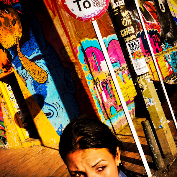 A Colombian girl walks around a street corner, covered in colorful graffiti artwork and posters, in La Candelaria, Bogota, Colombia.