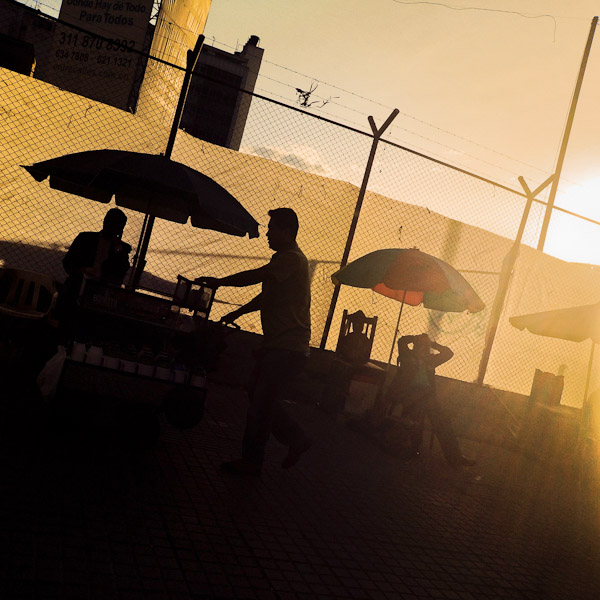 A Colombian street coffee vendor passes along shoe shiners during the twilight in Bogotá, Colombia.