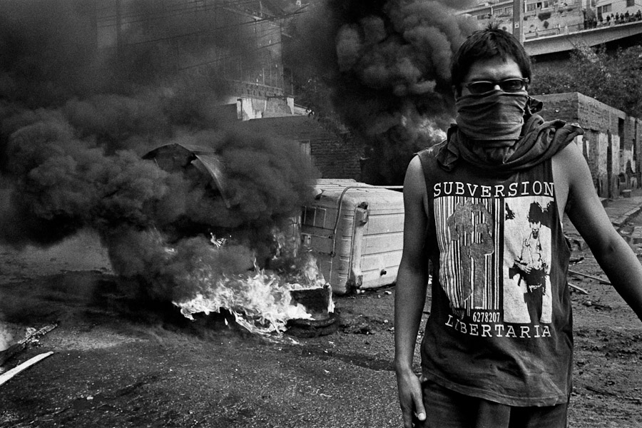 A Chilean student, having his face covered by a scraf, stands in front of the burning barricade during the anti-government protest in Valparaíso, Chile.