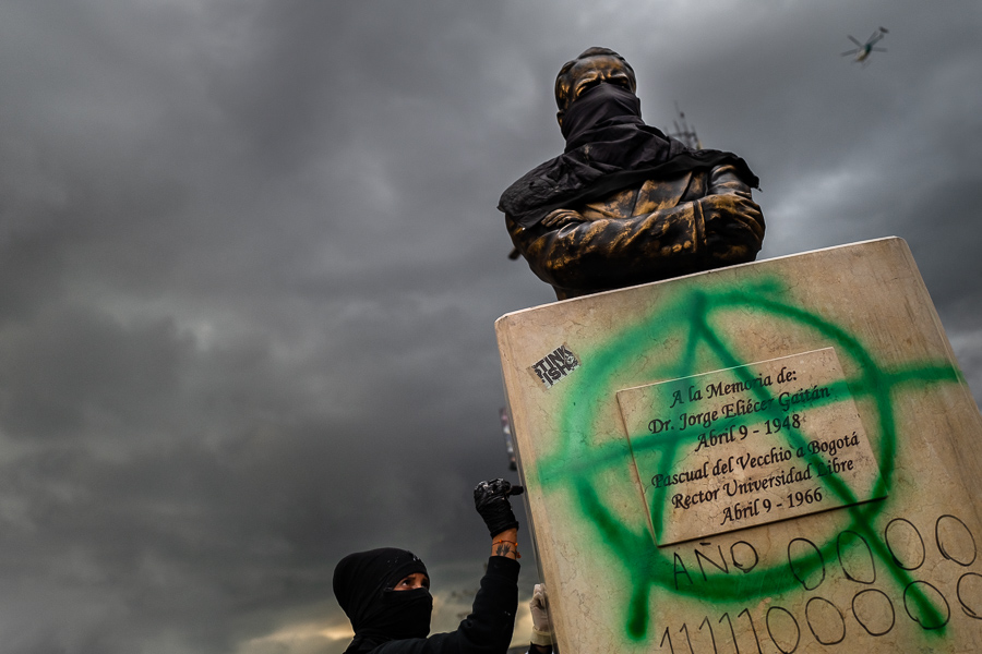 A radical student of the Universidad Nacional de Colombia writes a political slogan on a statue's pedestal during a protest march against government’s policies and corruption within the public educational system in Bogotá, Colombia.