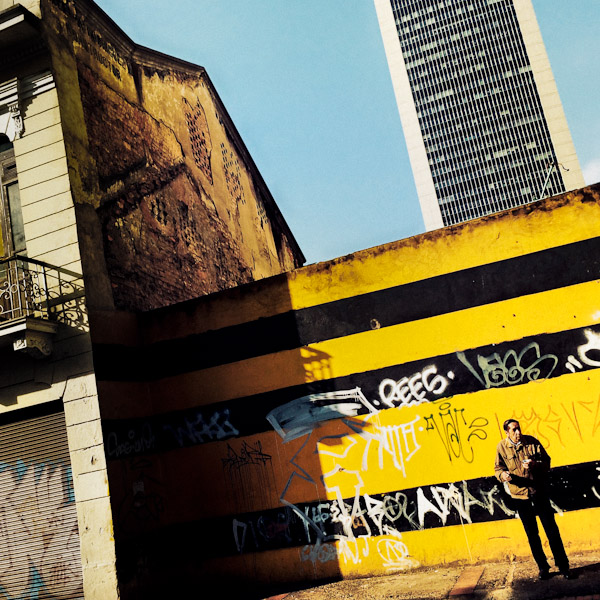 A Colombian man drinks coffee and smokes in front of a parking site wall, covered in territory tags, in Germania, Bogotá, Colombia.