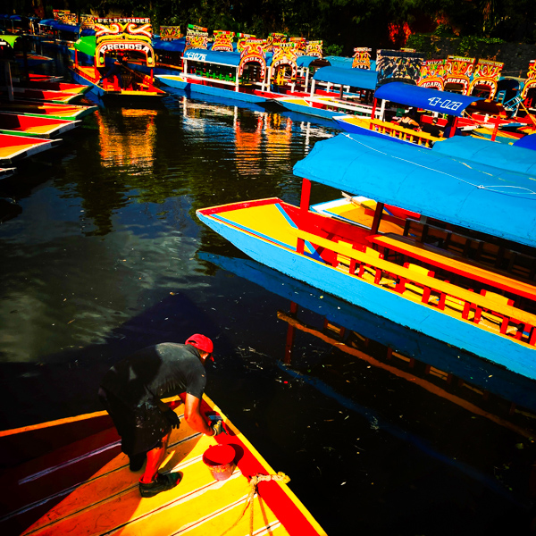 A Mexican gondolier repairs a colorfully painted wooden boat (Trajinera) used for boat ride trips on canals of Xochimilco in Mexico City, Mexico.