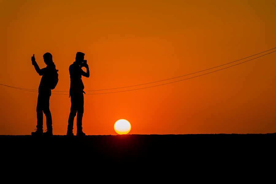 Young male tourists take selfie pictures on the stone walls, surrounding the colonial walled city, during the sunset in Cartagena, Colombia.