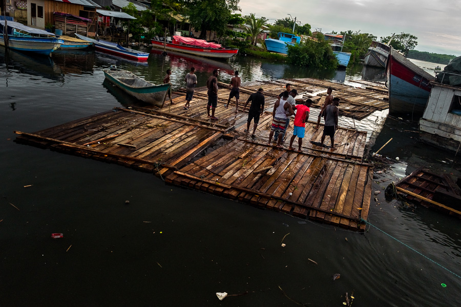 Afro-Colombian log drivers stand on a raft of rough sawn timbers floating in the water during wood transportation in the port of Turbo, Colombia.