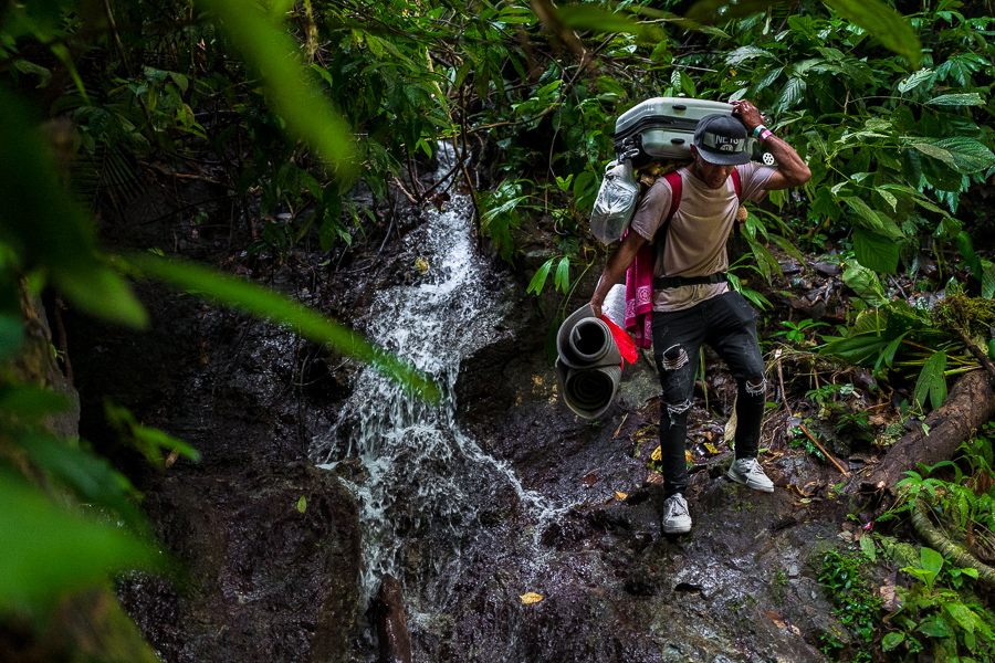 A Venezuelan migrant, carrying his family's luggage, climbs down a rocky trail alongside a waterfall in the wild and dangerous jungle of the Darién Gap between Colombia and Panamá.