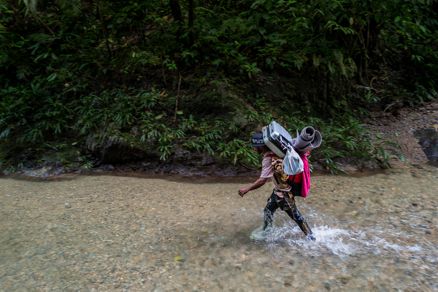 A Venezuelan migrant, carrying his family’s luggage, walks through the river in the wild and dangerous jungle of the Darién Gap between Colombia and Panamá.