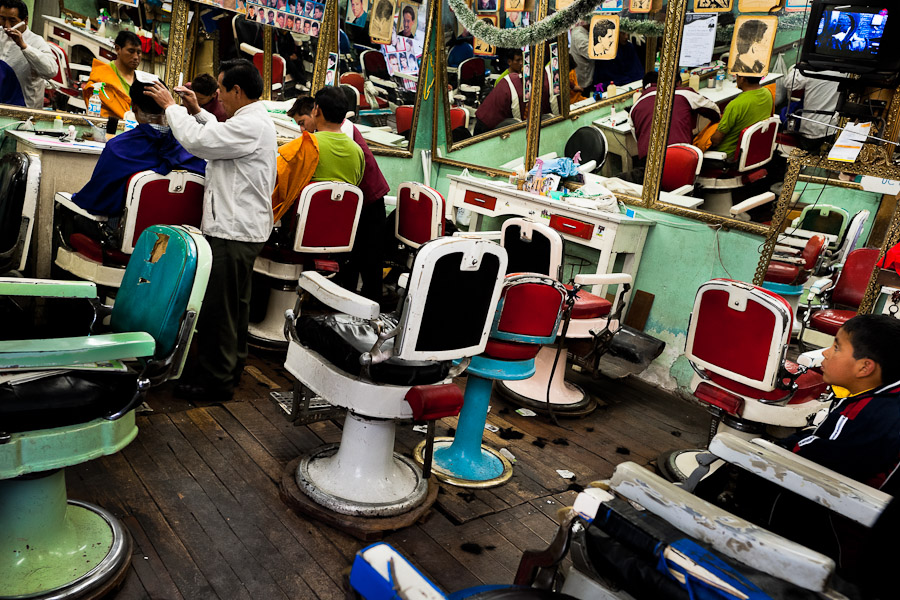 A Peruvian hairdresser cuts a man's hair in a vintage barber shop in Cuzco, Peru.