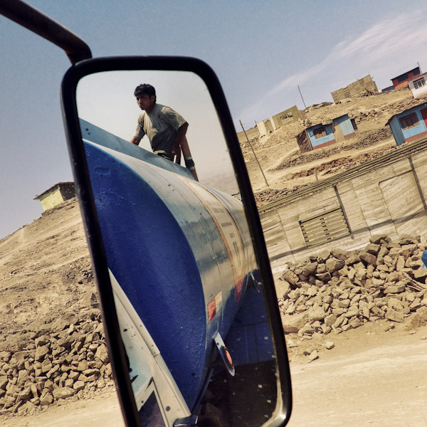 A Peruvian water distribution worker climbs up the water truck on the dusty hillsides of Pachacútec, a desert shantytown in Lima, Peru.