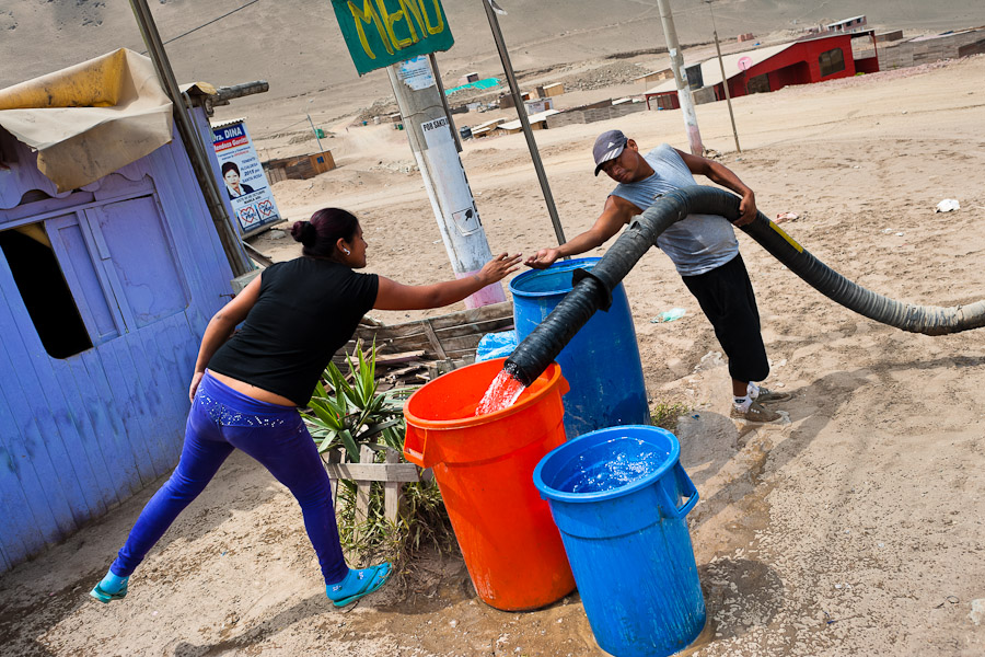 A Peruvian girl pays a water distribution worker to fill plastic barrels with drinking water on the dusty hillside of Pachacútec, a desert suburb of Lima, Peru.